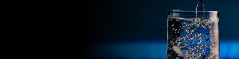 water pouring into a clear glass in front of a blue and black background