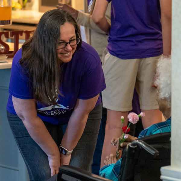 woman bends down to hand a flower to a senior resident at a nursing home in Silver Spring, Maryland