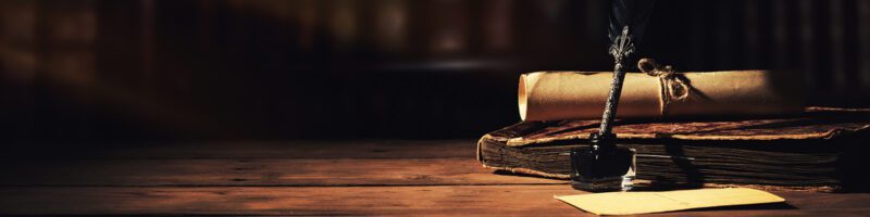 quill pen and parchment sitting on a rustic wood table