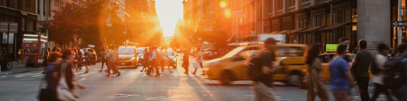 a busy street at sunset with taxi cabs and people in the crosswalk