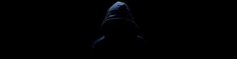 man with a hood in a shadowy dark background not wanting to be seen