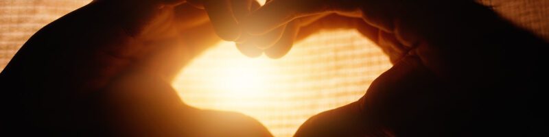 two hands forming a heart in front of a beautiful sunset